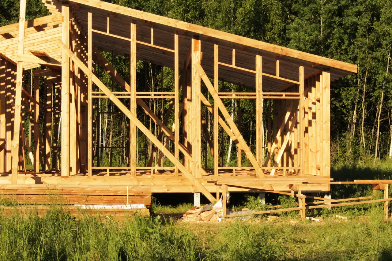 Timber house frame under construction beside a forest